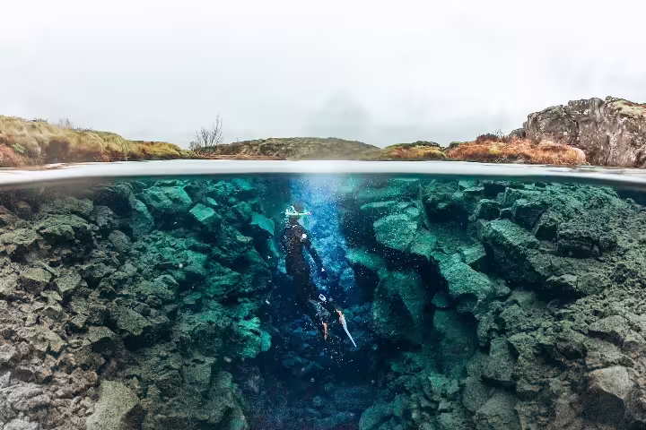 Snorkeler explores the clear waters of Silfra Fissure in Iceland, showcasing underwater volcanic rocks and stunning scenery.