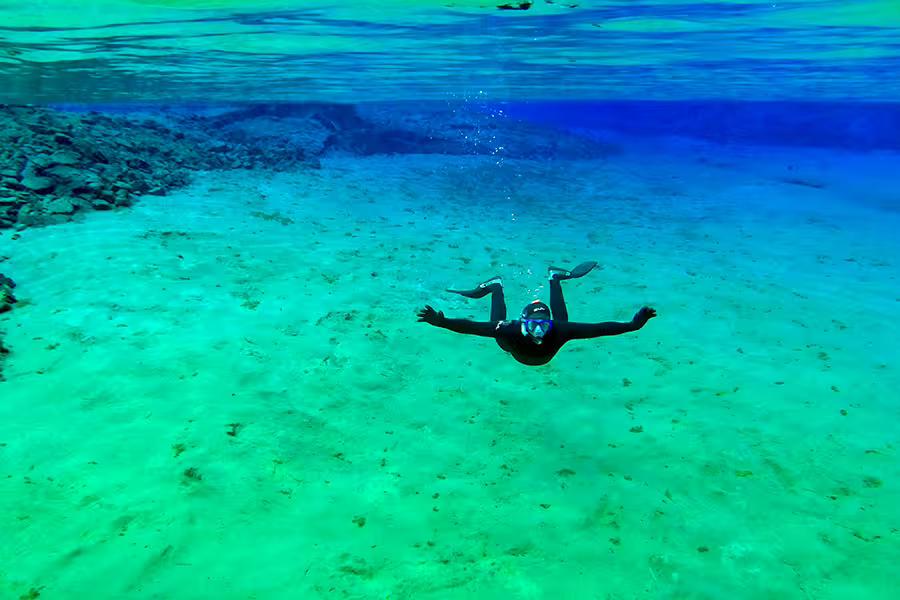 Snorkeler explores the crystal-clear waters of Silfra Fissure, showcasing unique underwater landscapes in Iceland.
