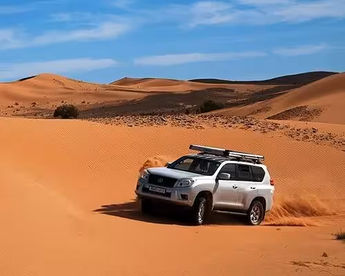 Silver 4x4 navigating vast sand dunes on an adventurous Rissani desert excursion under a clear blue sky.