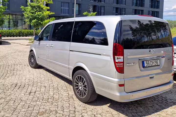 Silver minivan for private transfers between Porto and Lisbon, parked on cobblestone near modern buildings.