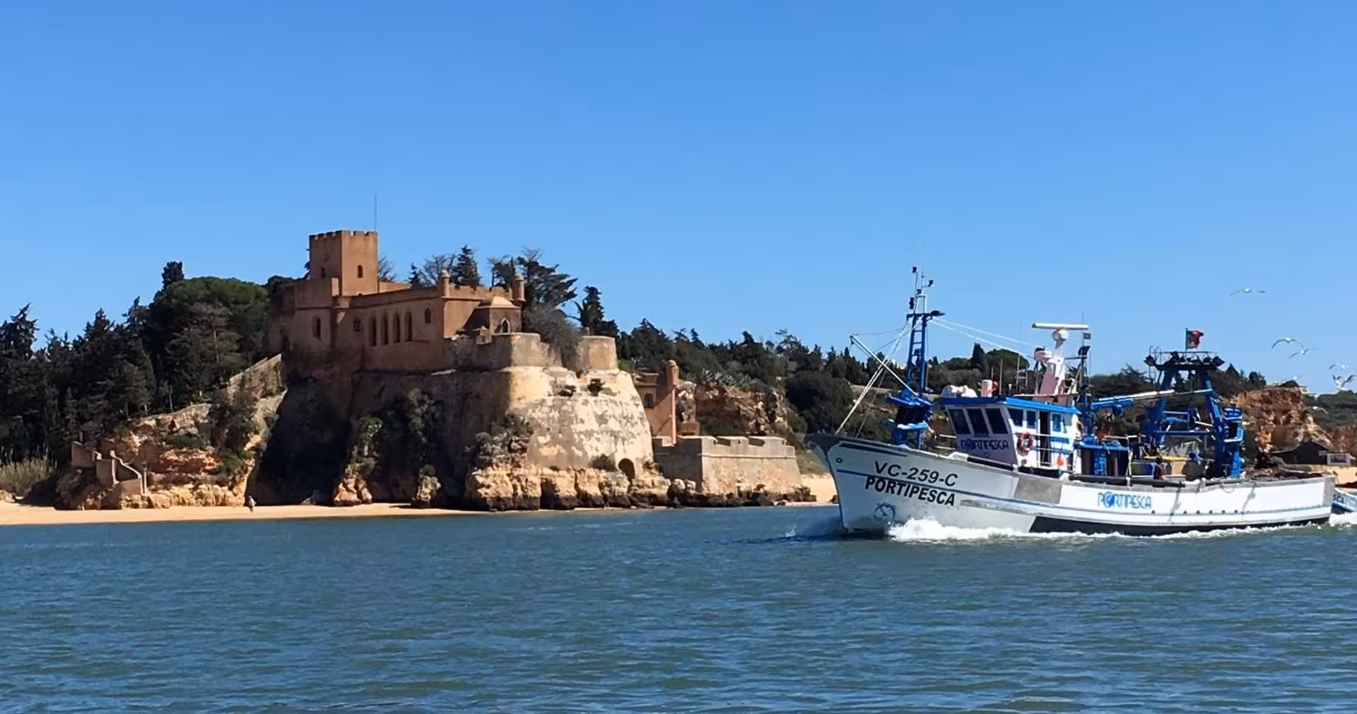 Fishing boat cruising past a historic riverside fortress on the Arade River near Silves on an Algarve sightseeing tour