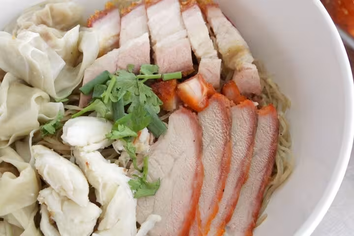 Assorted noodles with sliced pork and dumplings garnished with fresh herbs, part of the Singapore Chinatown Hawker Food Tour.