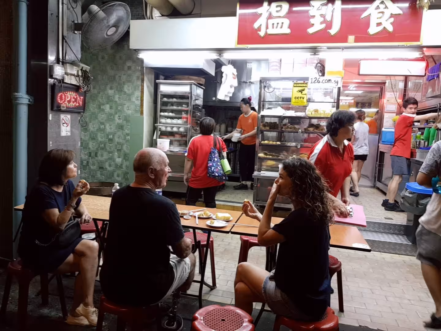 Tourists enjoy local street food at a vibrant Geylang eatery on the Singapore walking tour with free eSIM.