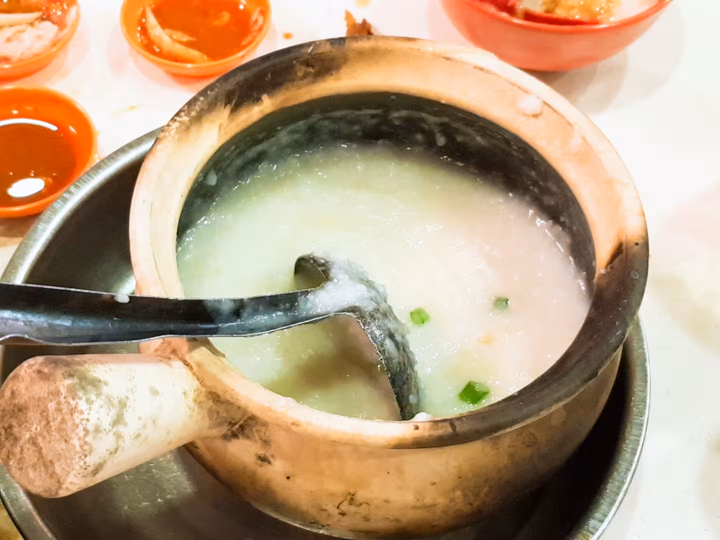 A steaming bowl of traditional porridge served in a clay pot, a highlight of the Geylang walking tour in Singapore.
