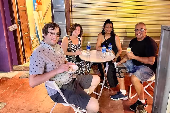 Visitors relaxing with drinks and snacks at a cozy Singapore street food spot, showcasing local dining culture.
