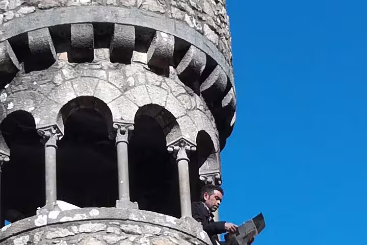Visitor reading map atop a historic stone tower under blue skies in Sintra on Cabo da Roca tour.