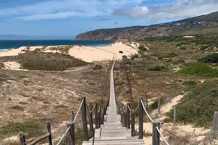Scenic boardwalk leading to a sandy beach in Sintra-Cascais Natural Park, highlighting the beauty of Portugal's coastline.