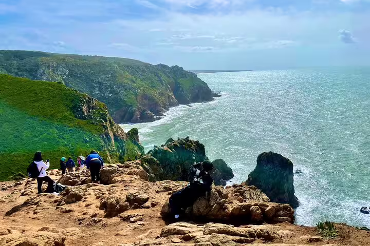 Tourists explore the rugged coastal cliffs of Sintra and Cascais, surrounded by stunning ocean views on a hidden gems tour.