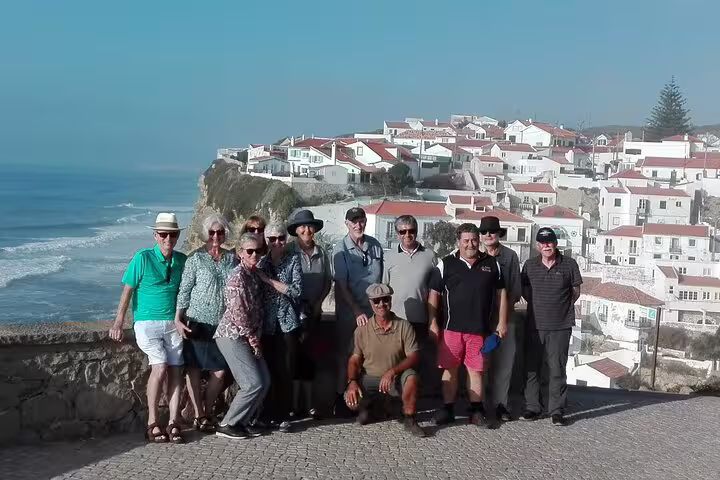 Tourists enjoy a scenic view of coastal cliffs and charming white houses on a Sintra half-day sightseeing tour from Lisbon.