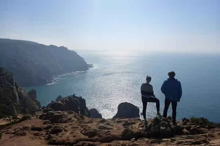Two people enjoy a stunning ocean view from a cliff on the Sintra World Heritage and Cascais Village Luxury Tour.