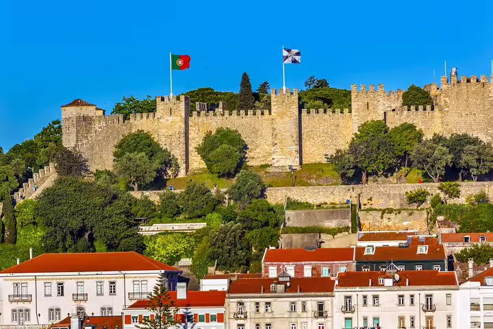 Majestic views of São Jorge Castle with Portuguese flags, perched above the historic red-roofed buildings of Lisbon.