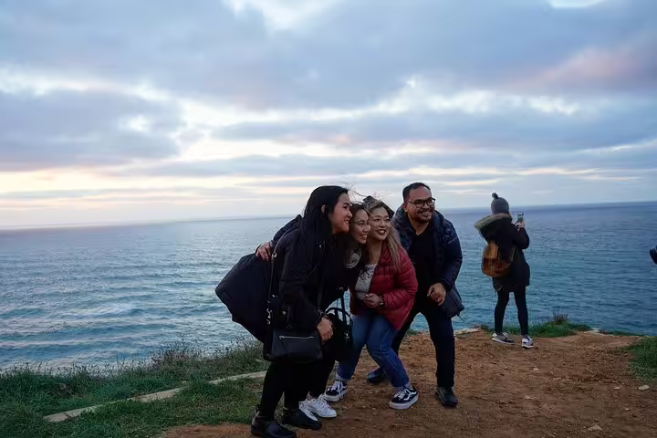 Tourists enjoying a scenic view on a Sintra half-day tour from Lisbon, overlooking the Atlantic Ocean at sunset.