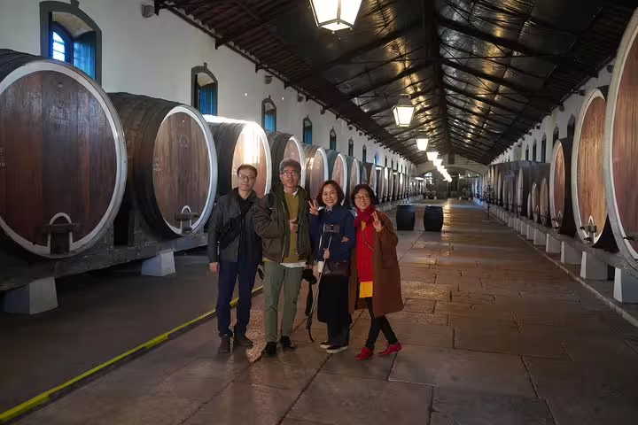 Group of tourists enjoying a wine cellar tour, part of the Sintra, Roca, and Cascais full-day private experience with Pena tickets.