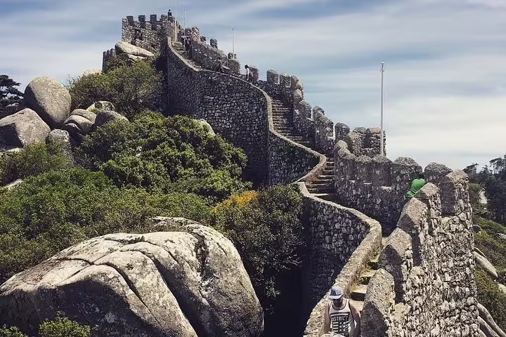 Ancient stone walls and lush greenery of the Castle of the Moors on a sunny day, part of Sintra's full-day tour attractions.