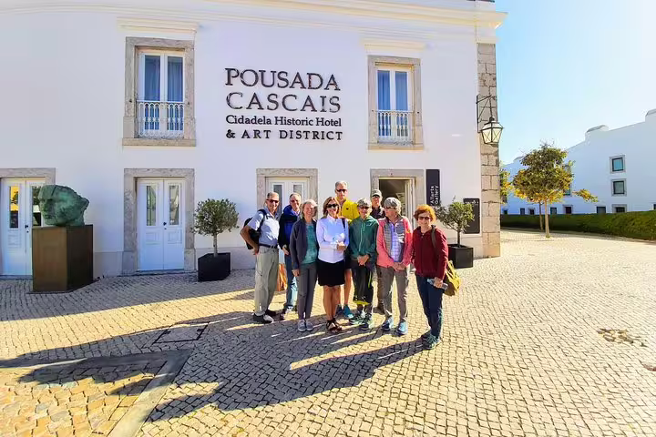 A group of tourists stands outside Pousada Cascais, part of the Sintra & Amazing Dream Villages Tour, in a sunny historic plaza.