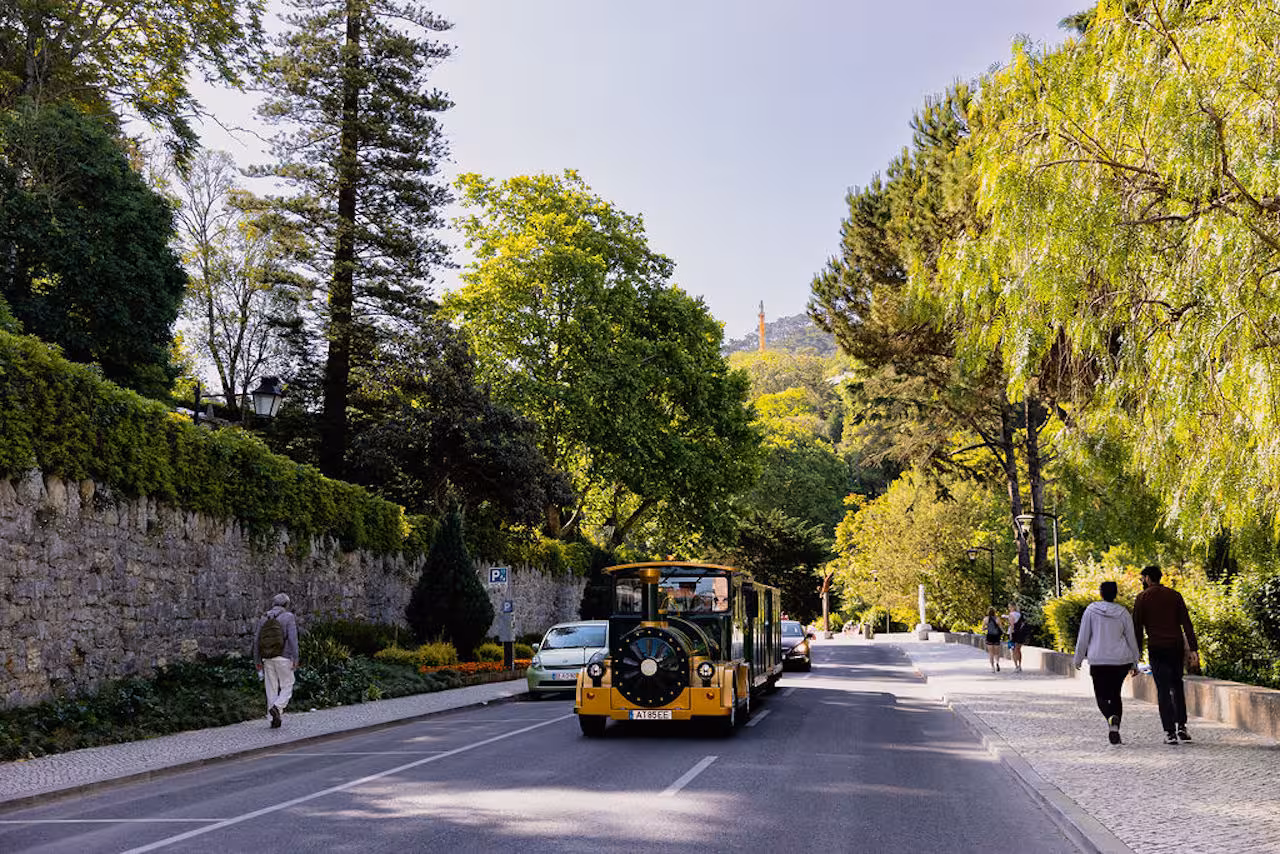 Sintra sightseeing road train passing gardens and stone walls, guided tour route to Pena Palace and Moorish Castle