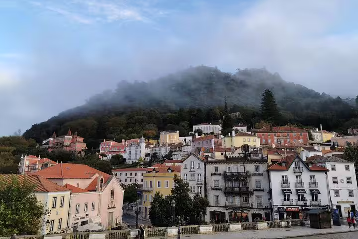 Colorful hillside view of Sintra's historic architecture under misty clouds, ideal for a private tour from Lisbon.