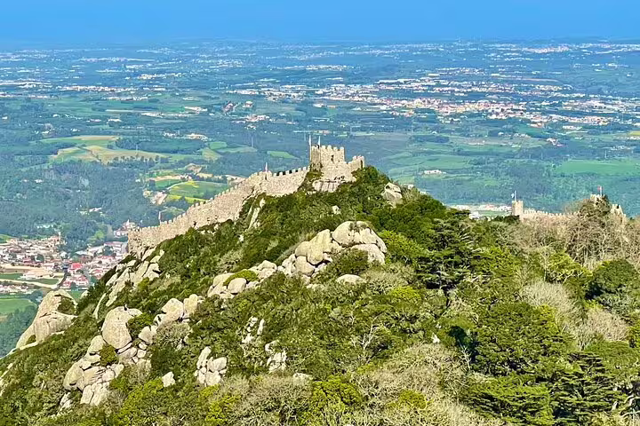 Scenic view of Sintra's Moorish Castle atop lush hills, showcasing the breathtaking landscape of the Sintra-Cascais region.