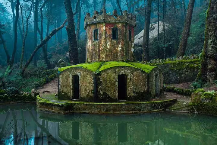 Moss-covered stone structure surrounded by lush forest and tranquil pond on a Sintra Mountain guided tour near Pena Palace.