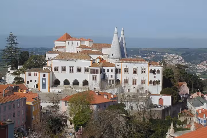 View of the historic National Palace of Sintra with its iconic chimneys and scenic surroundings on a sunny day.