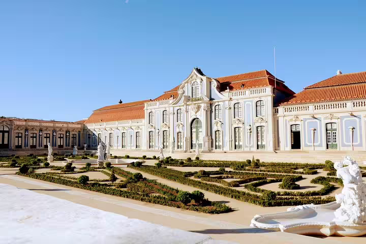 Exterior view of a grand palace with manicured gardens under a clear blue sky, featured in the Sintra and Cascais Village Tour.