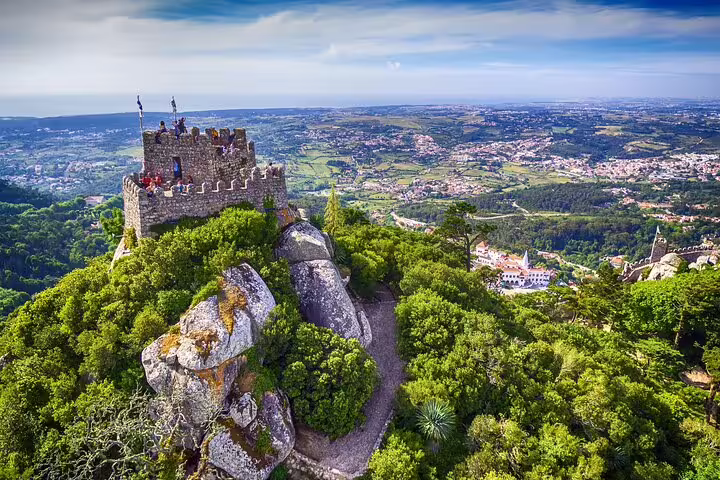 Aerial view of Sintra's medieval castle surrounded by lush greenery with panoramic landscapes, featured in our Lisbon full-day tour.