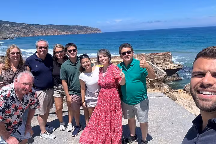 Happy travelers pose by the ocean in Cascais on a small group tour visiting Sintra, Pena Palace, and Cabo Roca.