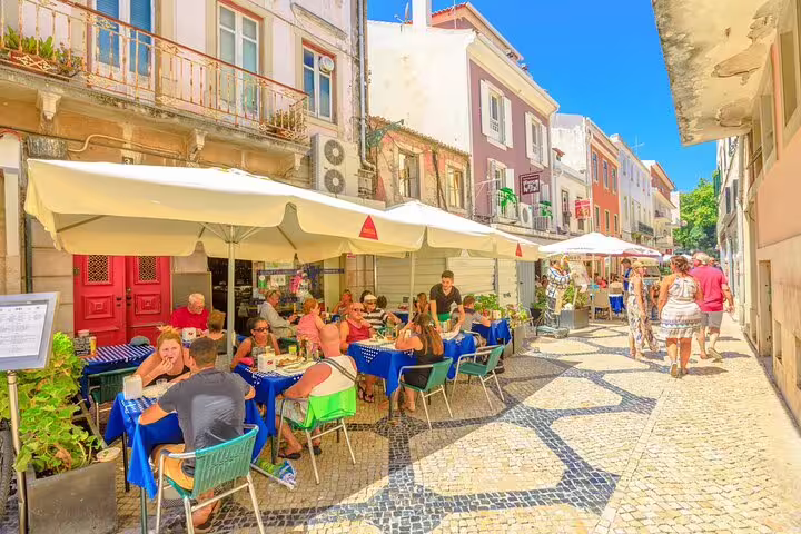 People enjoying outdoor dining at a charming café in Cascais during a sunny day on the Sintra and Pena Palace tour from Lisbon.
