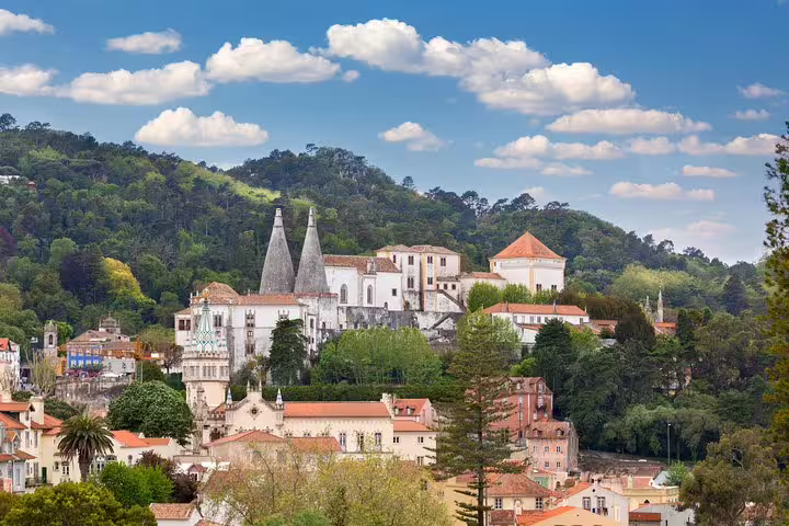 View of Sintra's historic architecture and lush hills, featuring the iconic chimneys of the National Palace on a sunny day.