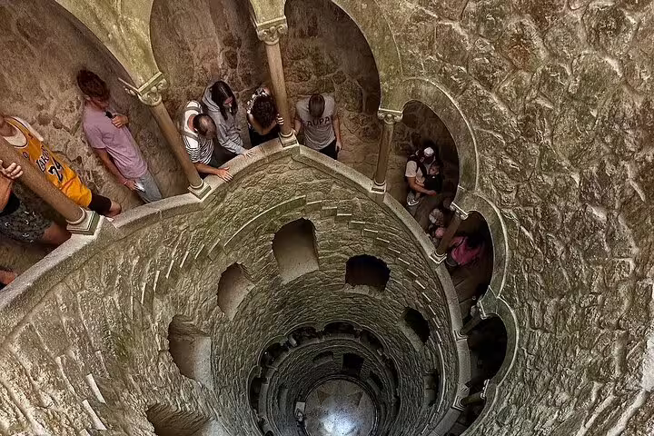 Tourists explore the enchanting spiral staircase of the Initiation Well at Quinta da Regaleira on a Sintra and Pena Palace tour.
