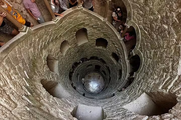 Tourists explore the enchanting spiral staircase of the Initiation Well at Quinta da Regaleira during a Sintra full-day tour.