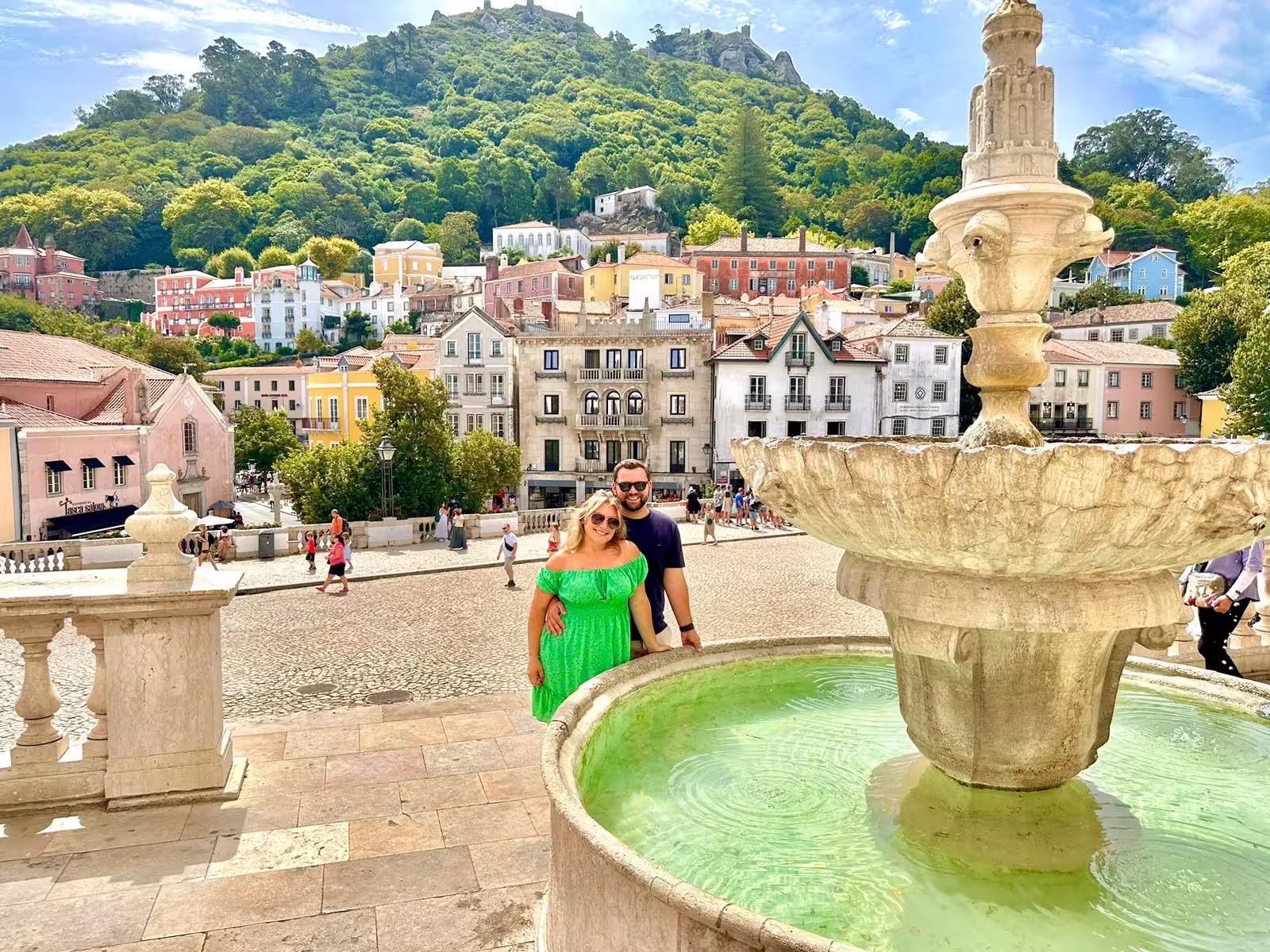 Scenic view of Sintra's colorful village and fountain with lush hills in the background, perfect for Pena Palace tour.