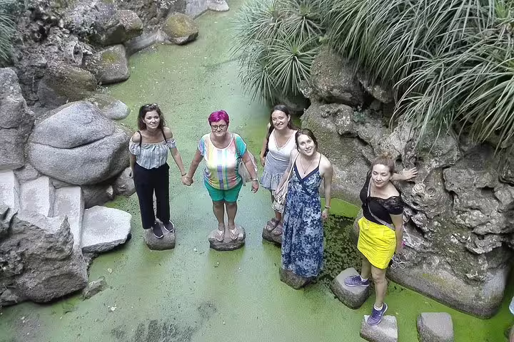 Group of tourists enjoy stepping stones over a lush green pond in Sintra during a full-day private tour with Pena Palace tickets.