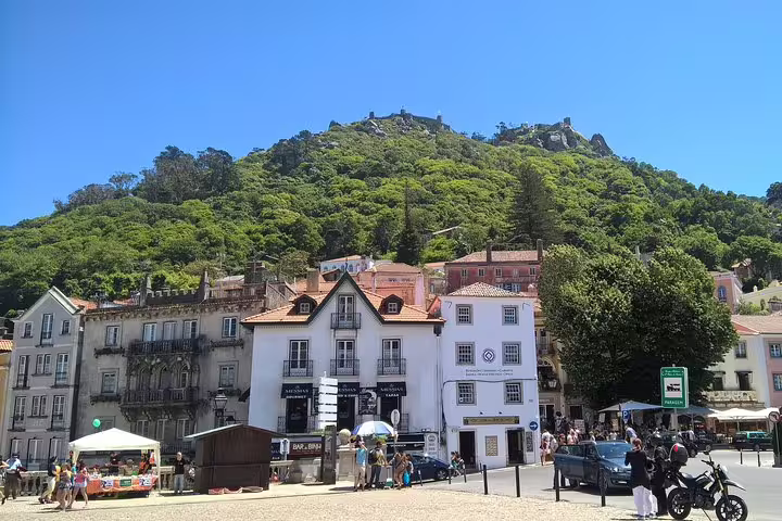 Bustling Sintra town square with historic buildings and lush green hills under a clear blue sky, perfect for private tours.