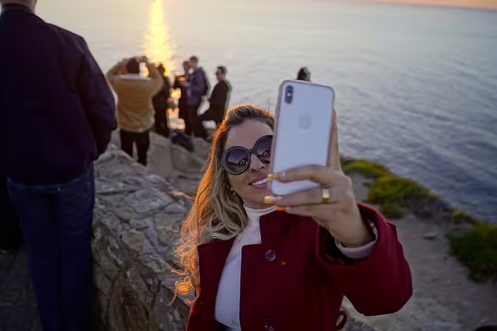 Traveler takes a selfie at sunset by the ocean during a Sintra, Roca, and Cascais full-day private tour experience.