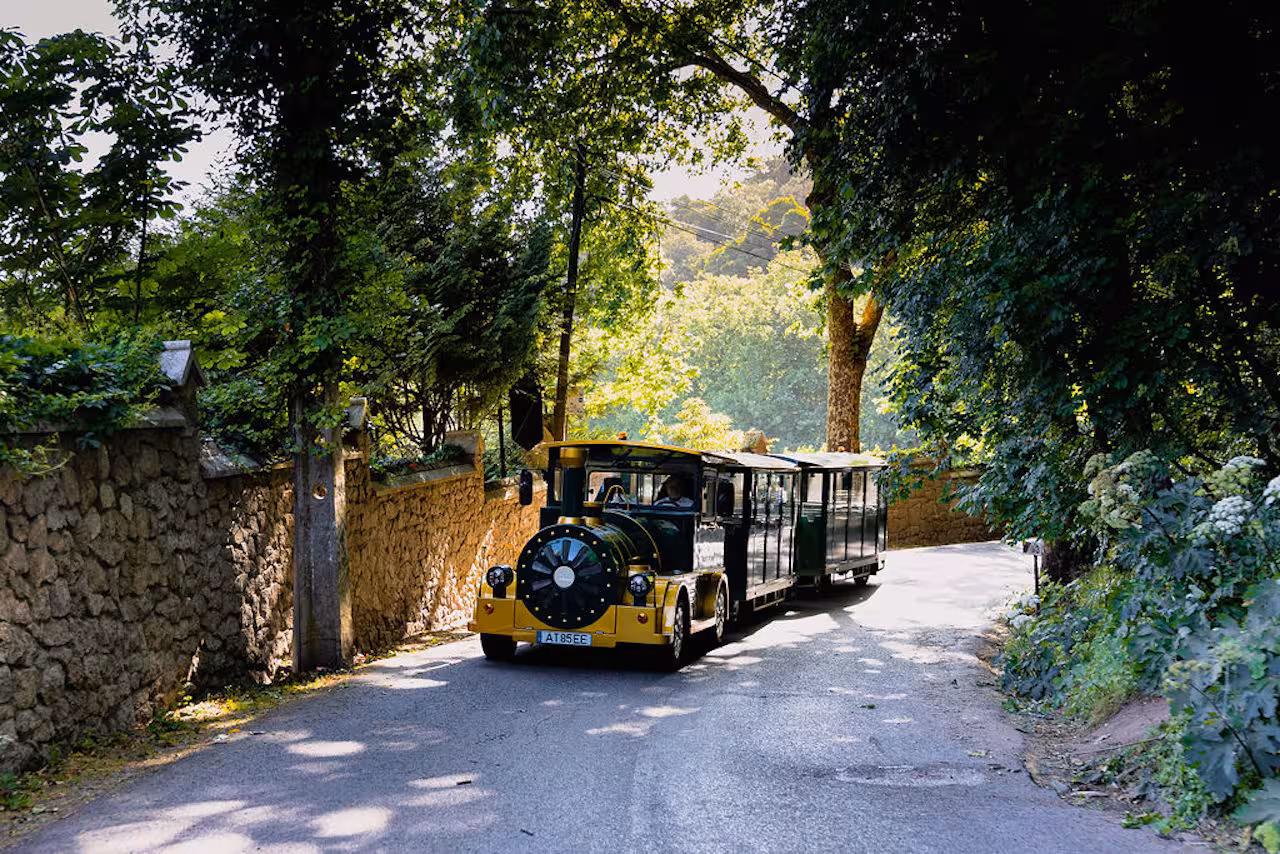 Sintra tourist train on a shaded forest road, scenic guided tour transport to top Sintra landmarks in Portugal
