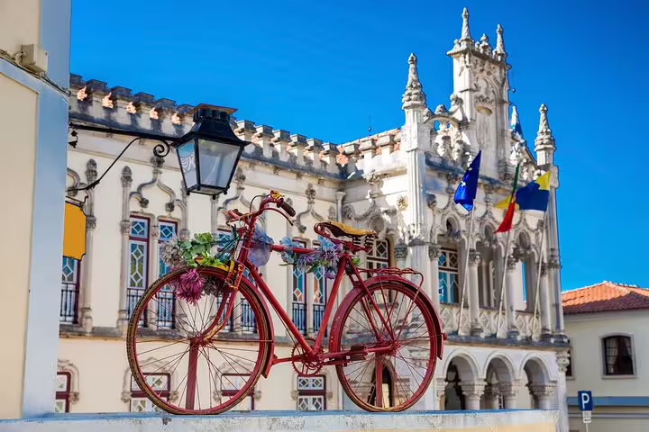 Red vintage bicycle adorned with flowers in front of ornate architecture in Sintra, featured on private tour with Regaleira tickets.