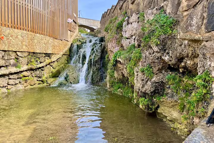 Scenic view of a tranquil waterfall cascading over mossy rocks in Sintra, highlighting nature's charm on a private wine tour.