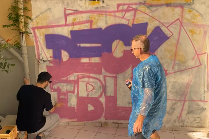 Guests spray-paint bold graffiti letters during Sip and Spray locals tour, cocktails and street art workshop