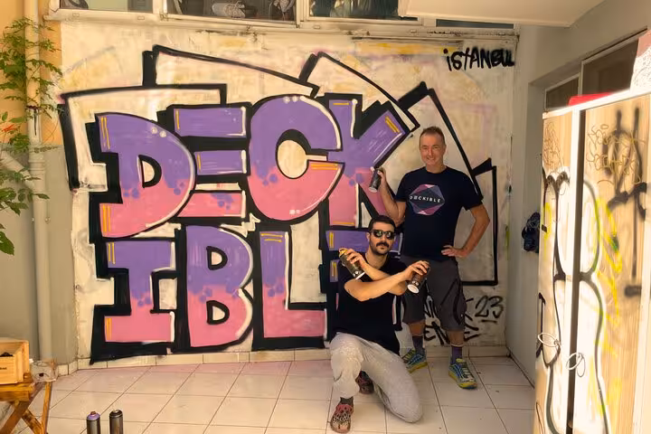 Participants pose with finished graffiti mural holding spray cans on Sip and Spray with locals cocktail tour