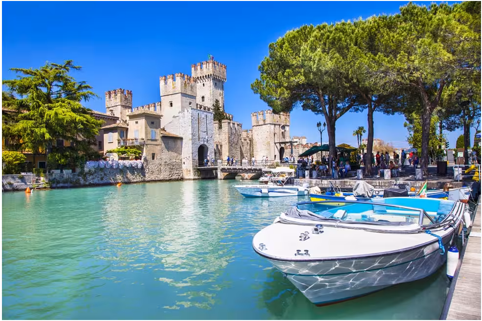 Scenic view of Sirmione Castle by Lake Garda with boats and lush greenery, perfect for a day trip from Milan.