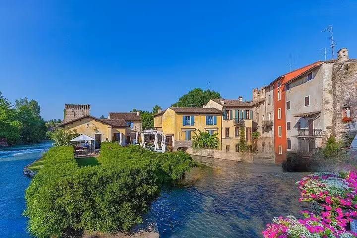 Scenic view of colorful riverside houses and lush greenery in Sirmione, ideal for a private day tour from Venice.