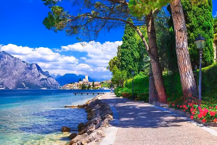 Scenic lakeside walkway in Sirmione with lush greenery and clear blue waters, perfect for relaxation on a day trip from Venice.