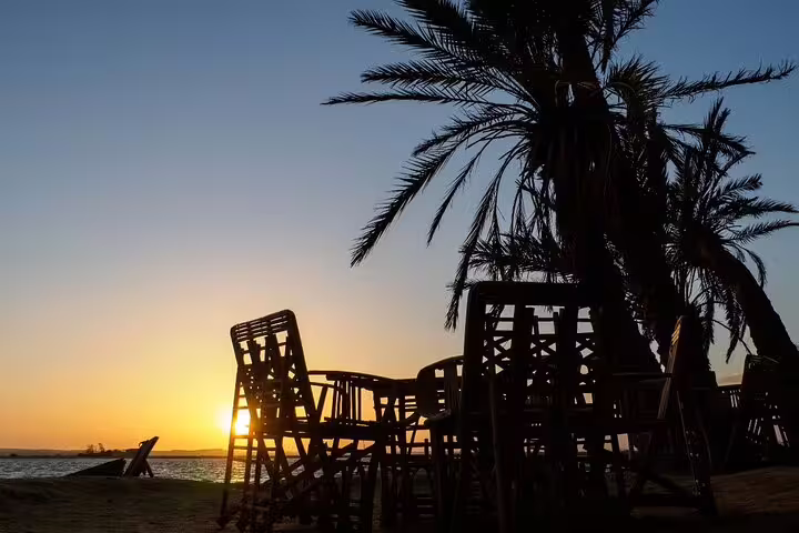 Sunset by a Siwa Oasis lake with palm trees and rustic chairs, part of a 4-day private tour from Cairo