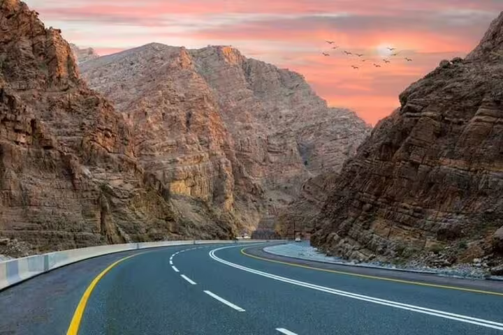 Scenic mountain road at sunset with birds in the sky, featured in the Six Emirates Tour from Dubai.