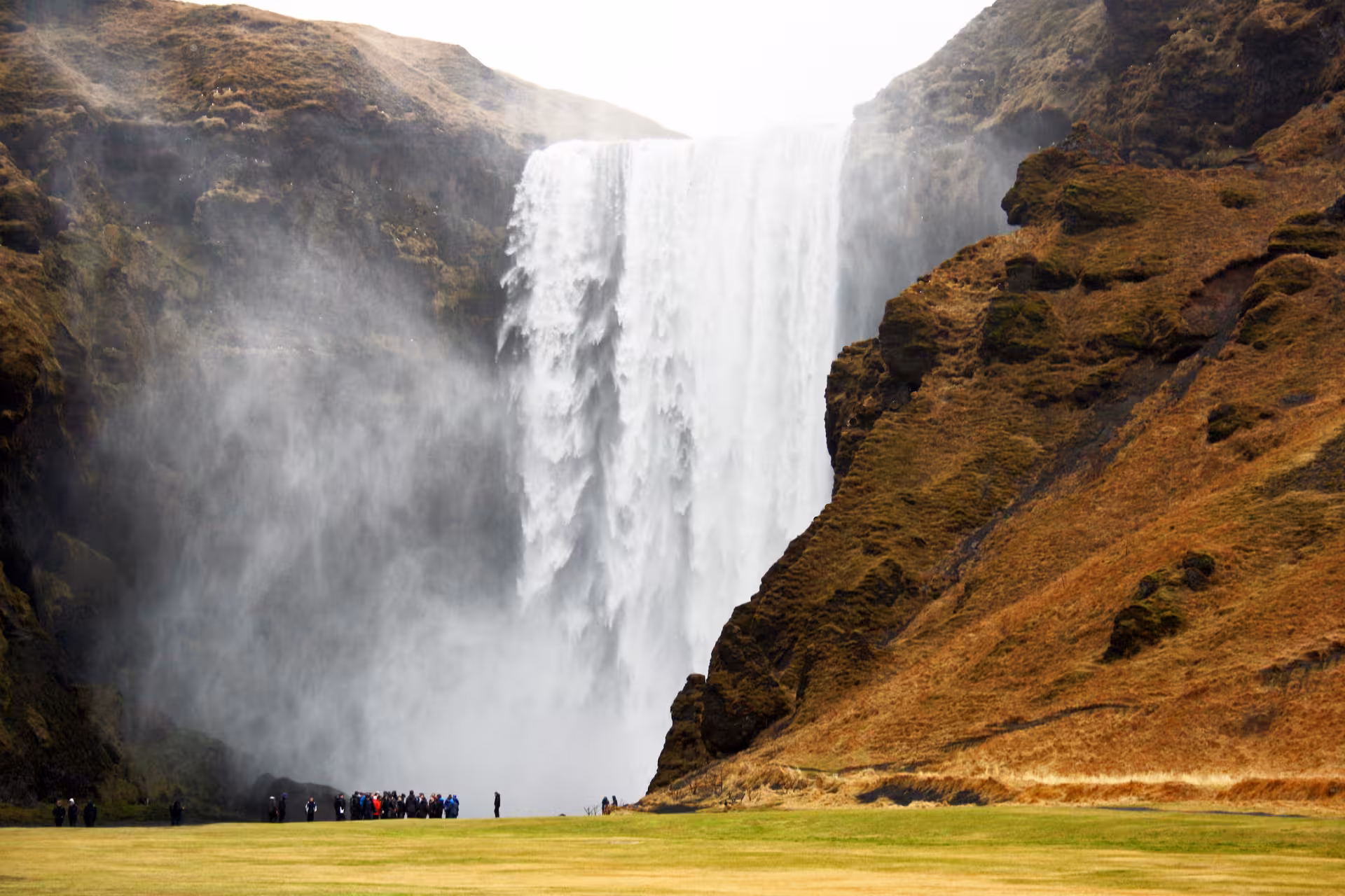 Visitors gather at the base of Skógafoss waterfall, surrounded by lush landscapes on a South Coast tour in Iceland.