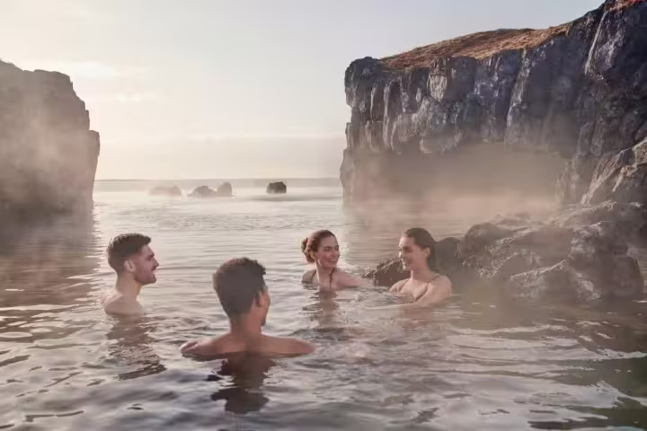 People enjoying a relaxing soak in the Sky Lagoon's geothermal waters, surrounded by rocky cliffs and misty atmosphere in Iceland.