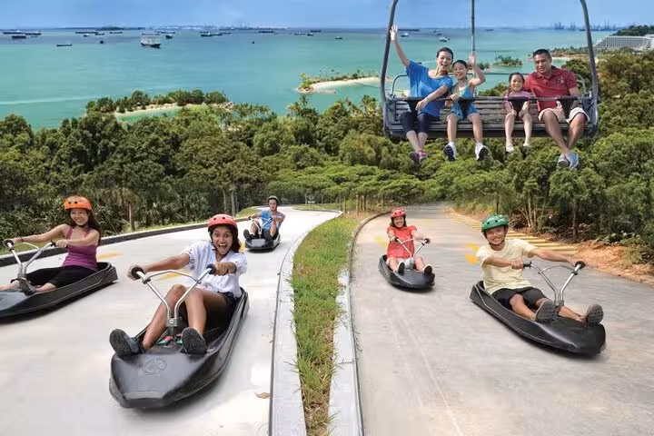 Skyline Luge Sentosa Singapore with riders racing downhill and Skyride chairlift over sea views, tickets