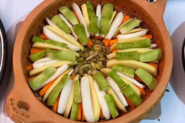 Vibrant sliced vegetables arranged in a traditional clay pot ready for cooking in a family-style culinary class.