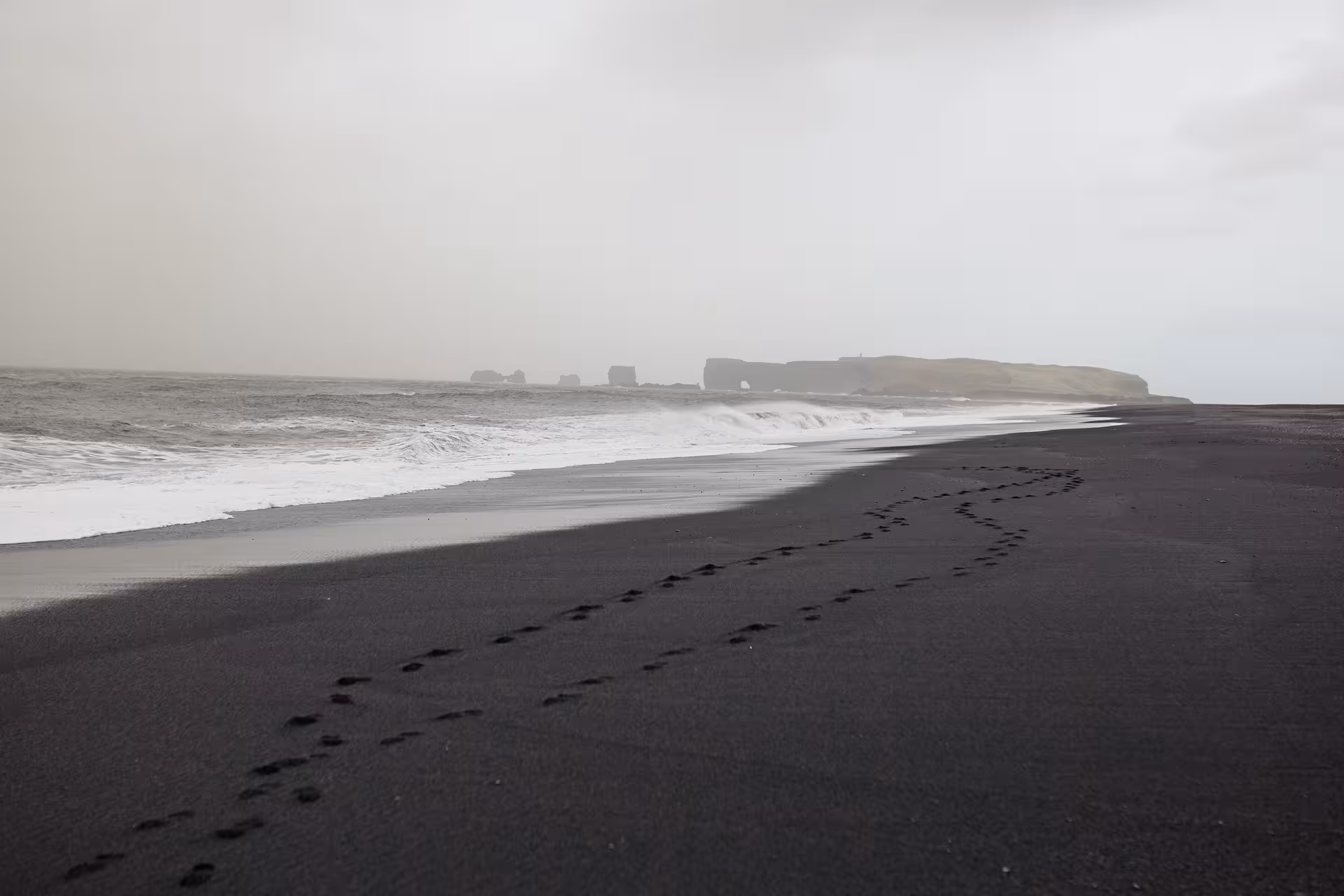 Black sand beach with ocean waves and distant cliffs on Snæfellsnes Peninsula, perfect for a private day tour.